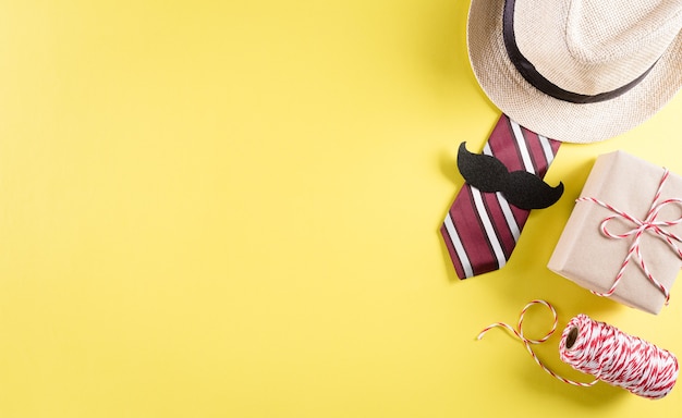 Concetto di sfondo per la festa del papà felice con cravatta e baffi, cappello, confezione regalo su sfondo giallo pastello.