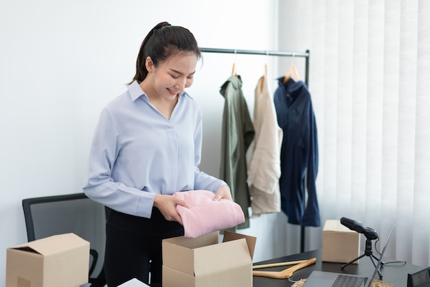 Concetto di shopping dal vivo un commerciante femminile che imballa i prodotti in scatole dopo aver ricevuto ordini dai clienti.