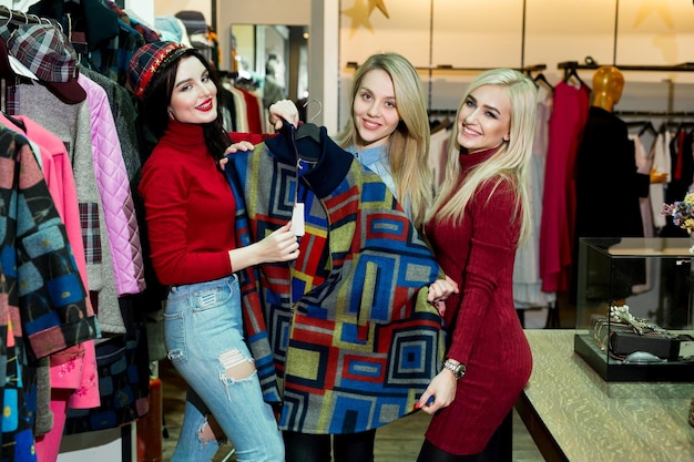 Concetto di shopping, moda e amicizia - tre amici sorridenti che provano alcuni vestiti al centro commerciale.