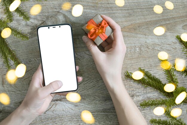 Concetto di shopping online di Natale La donna acquista regali con il telefono cellulare si prepara al Natale con una confezione regalo in mano Saldi per le vacanze invernali