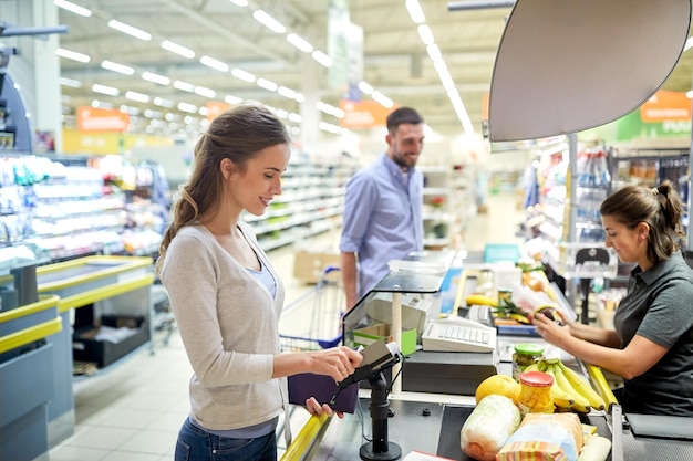 concetto di shopping, vendita, consumismo e persone - coppia felice che compra cibo al supermercato o al registratore di cassa del supermercato e fa scorrere la carta cliente