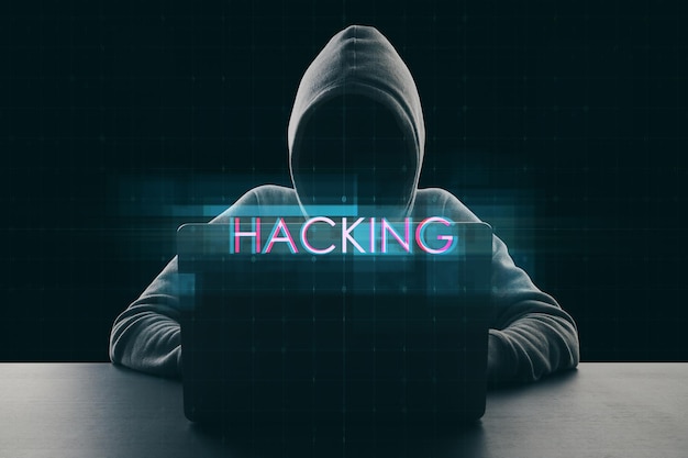 Concetto di sicurezza informatica e protezione dei dati con segno di hacking digitale e hacker senza volto in felpa con cappuccio che utilizza laptop su sfondo scuro