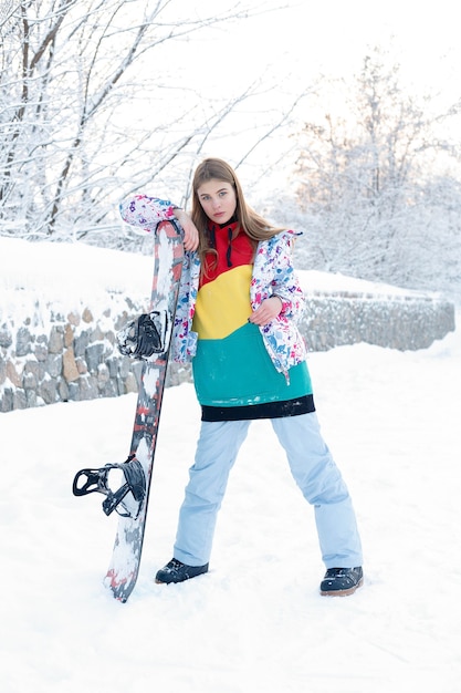 Concetto di snowboard all'aperto di inverno della donna. Giovane donna che tiene lo snowboard sulle spalle, guarda lontano e sorride, copia spazio, primo piano