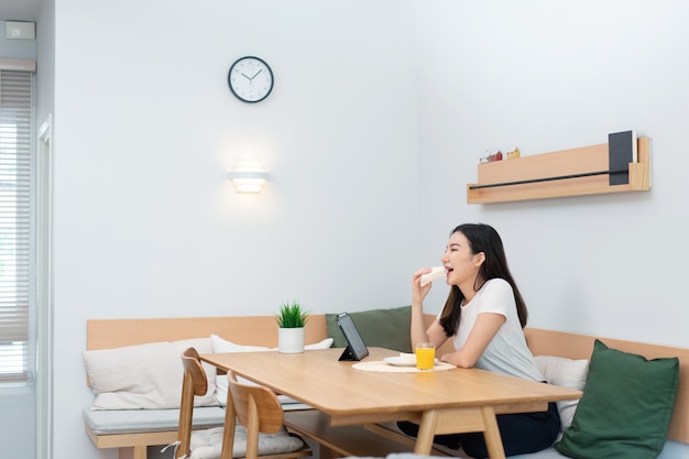 Concetto di soggiorno una femmina adulta che si diverte a mangiare panini e succo d'arancia guardando i media online durante la pausa di lavoro.