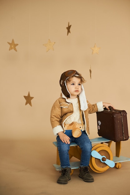 Concetto di sogni e viaggi. pilota pilota bambino aviatore con un aeroplanino giocattolo e giochi valigia in una superficie beige