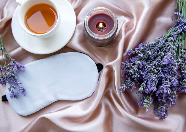 Concetto di sonno sano. Bouquet di lavanda, maschera per dormire e candela su sfondo di seta