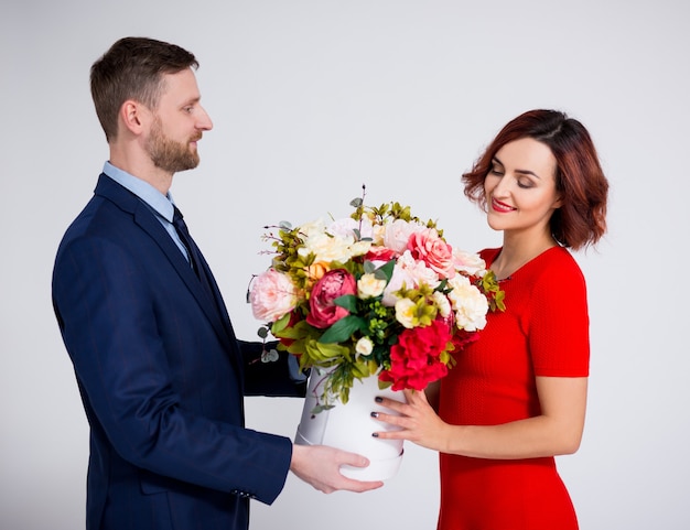 Concetto di sorpresa di San Valentino o compleanno - bell'uomo che sorprende la sua ragazza con fiori su sfondo bianco