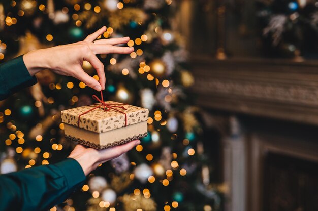 Concetto di sorpresa e momenti piacevoli La donna avvolge il regalo di Capodanno come stand in soggiorno vicino a un bellissimo abete decorato Vacanze x mas e concetto di celebrazione