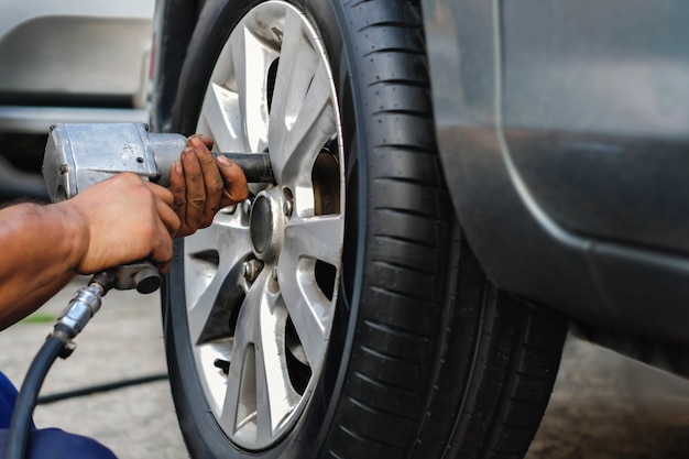 Concetto di sostituzione della gomma. Meccanico che utilizza la chiave elettrica del cacciavite per i dadi della ruota in garage. Manutenzione e servizi dell&#39;automobile