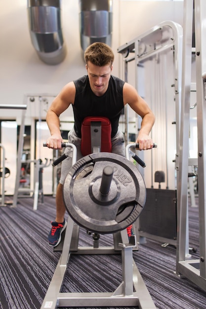 concetto di sport, bodybuilding, attrezzature e persone - giovane con bilanciere che flette i muscoli sulla macchina a t-bar in palestra