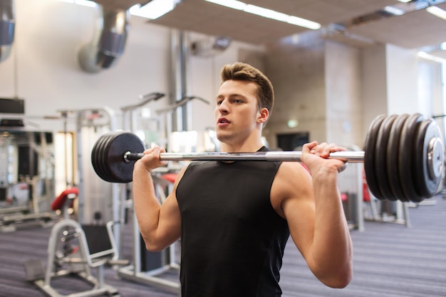 concetto di sport, bodybuilding, stile di vita e persone - giovane con bilanciere che flette i muscoli in palestra