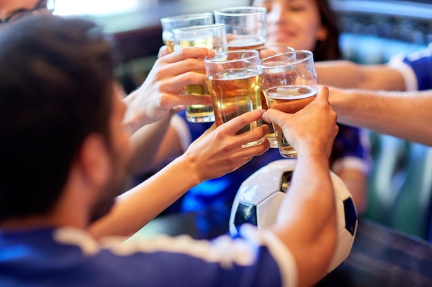 concetto di sport, calcio, persone e tempo libero: amici felici o appassionati di calcio che tintinnano bicchieri di birra al bar o al pub