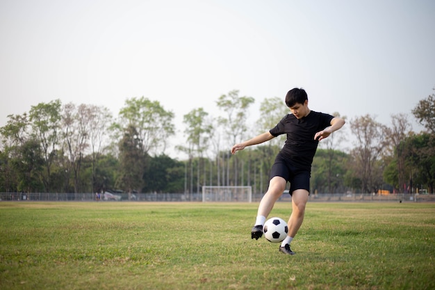 Concetto di sport e ricreazione un giocatore di calcio maschile che indossa una maglietta nera e pantaloni che si esercitano a calciare la palla nel campo erboso.