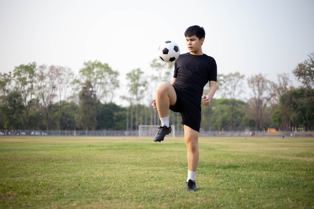 Concetto di sport e ricreazione un giocatore di calcio maschile che indossa una maglietta nera e pantaloni che si esercitano a calciare la palla nel campo erboso.