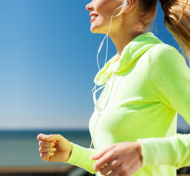 concetto di sport e stile di vita sano - donna che corre e ascolta musica con gli auricolari all'aperto