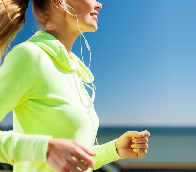 concetto di sport e stile di vita sano - donna che corre e ascolta musica con gli auricolari all'aperto