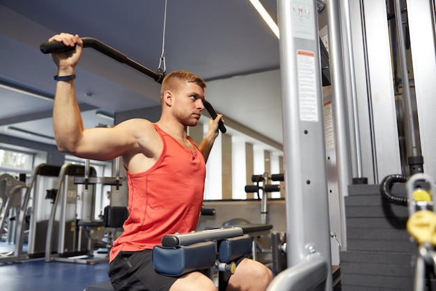 concetto di sport, fitness, bodybuilding, stile di vita e persone - uomo che esercita e flette i muscoli sulla macchina via cavo in palestra