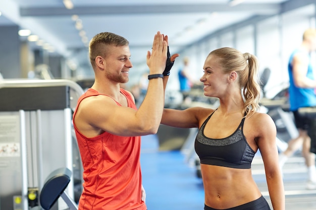 concetto di sport, fitness, stile di vita, gesto e persone - uomo e donna sorridenti che fanno il cinque in palestra