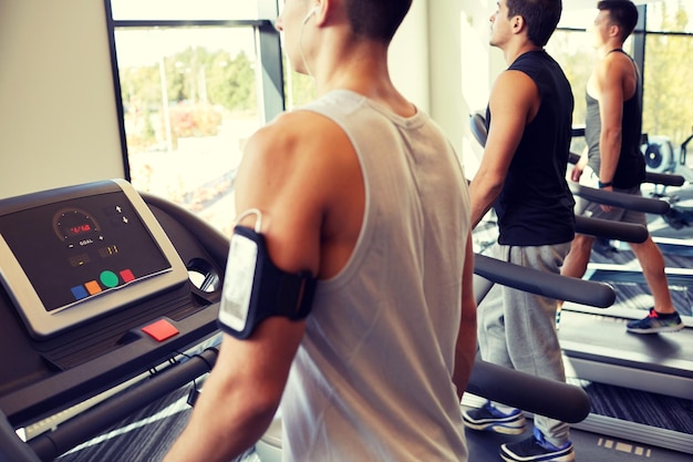 concetto di sport, fitness, stile di vita, tecnologia e persone - uomini sorridenti che si esercitano sul tapis roulant in palestra