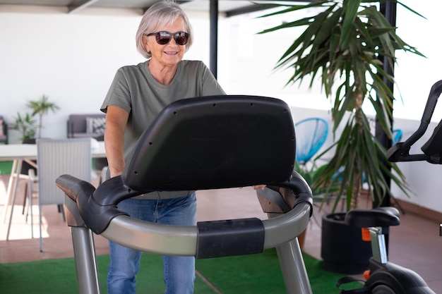 Concetto di sport per le persone Felice donna anziana che fa esercizi per mantenersi in forma correndo sul tapis roulant in terrazza