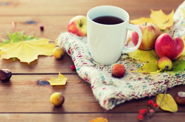 concetto di stagione, bevanda e mattina - primo piano della tazza di tè sul tavolo di legno con foglie autunnali e sciarpa