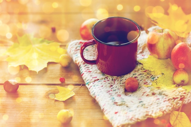 concetto di stagione, bevanda e mattina - primo piano della tazza di tè sul tavolo di legno con foglie autunnali e sciarpa