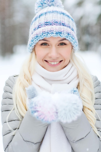 concetto di stagione, natale e persone - giovane donna sorridente felice che tiene la neve sulle palme nella foresta d'inverno