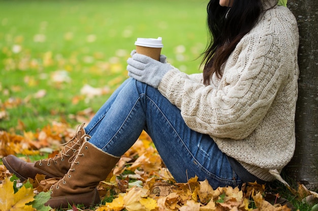 concetto di stagione, tecnologia e persone - primo piano di giovane donna che beve caffè dalla tazza di carta nel parco autunnale