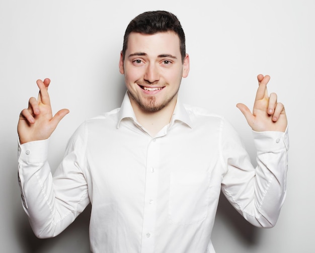 Concetto di stile di vita, affari e persone: uomo d'affari in camicia che tiene le dita incrociate in piedi su sfondo bianco