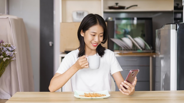 Concetto di stile di vita domestico Giovane donna che beve caffè e naviga sui social media sullo smartphone a casa