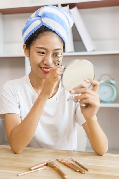 Concetto di stile di vita domestico Giovane donna in turbante dopo la doccia e ciglia arricciate per il trucco a casa