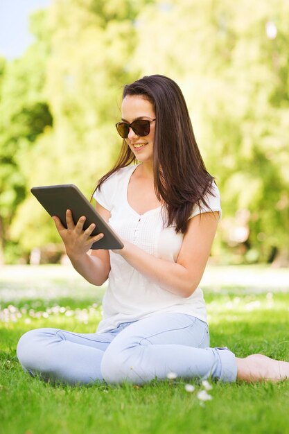 concetto di stile di vita, estate, vacanze, tecnologia e persone - ragazza sorridente con tablet pc seduto sull'erba nel parco