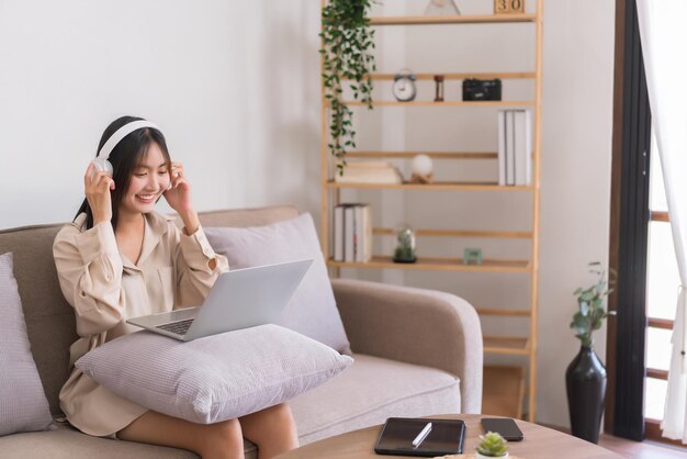 Concetto di stile di vita rilassante La giovane donna asiatica indossa le cuffie e ascolta musica sul laptop