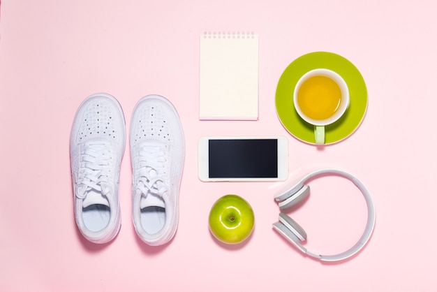 Concetto di stile di vita sano. Scarpe da ginnastica, tè, mela e cuffie su sfondo color pastello.