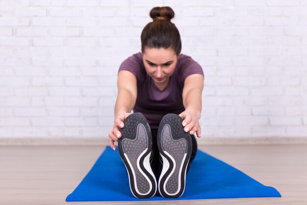 Concetto di stile di vita sano - vista frontale della giovane donna che fa esercizio di stretching sulla stuoia di yoga