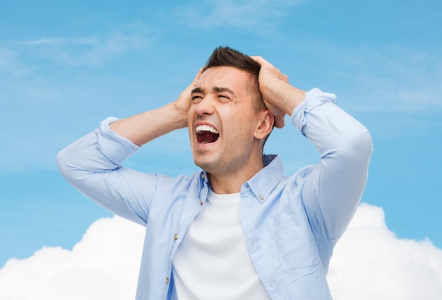 concetto di stress, mal di testa, assistenza sanitaria e persone - uomo infelice con gli occhi chiusi che si tocca la fronte sopra il cielo blu e lo sfondo delle nuvole