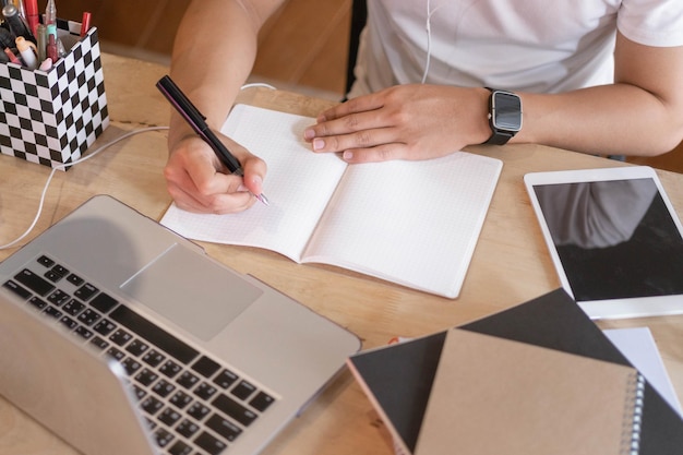 Concetto di studio online il classico uomo con maglietta bianca impegnato a cercare di finire i suoi progetti, il che rende la sua scrivania disordinata con iPad, laptop e libri.