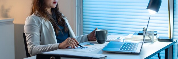 Concetto di superlavoro La donna dell'ufficio che lavora alla sua scrivania puntando la penna sulla carta