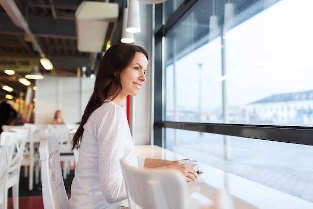 concetto di svago, bevande, persone e stile di vita - giovane donna sorridente che beve caffè al bar