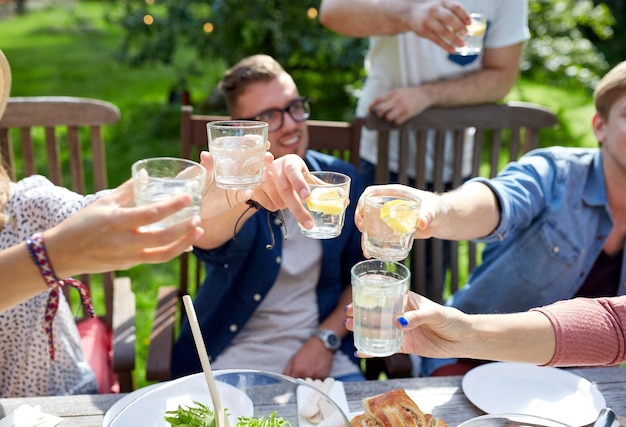 Concetto di svago, di feste, di cibo, della gente e dell&#39;alimento - amici felici cenando alla festa in giardino dell&#39;estate e bevande clinking