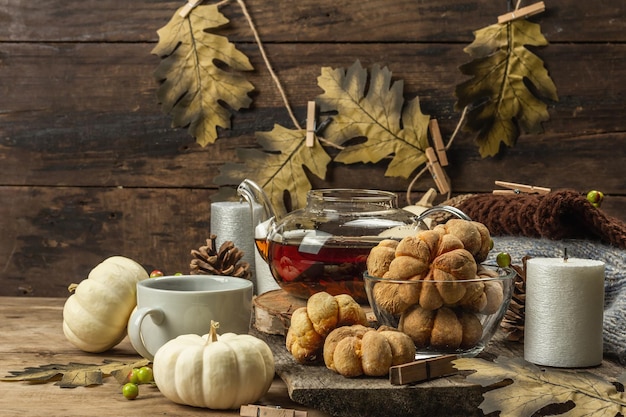 Concetto di tè autunnale. Biscotti con purea di zucca, tè nero in una teiera di vetro, decorazioni autunnali. Ghirlanda, candele, un maglione accogliente. Vecchio fondo in legno, copia spazio