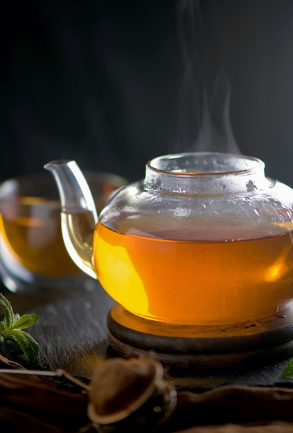 Concetto di tè, teiera con tè circondato su una superficie di legno, cerimonia del tè, tè verde in una tazza trasparente