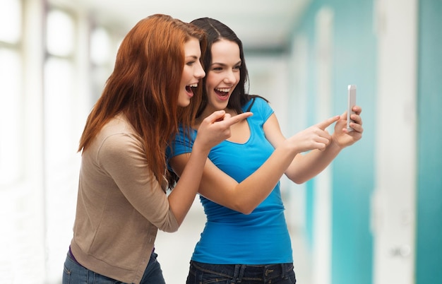 concetto di tecnologia, amicizia e persone - due adolescenti sorridenti che puntano il dito contro lo smartphone