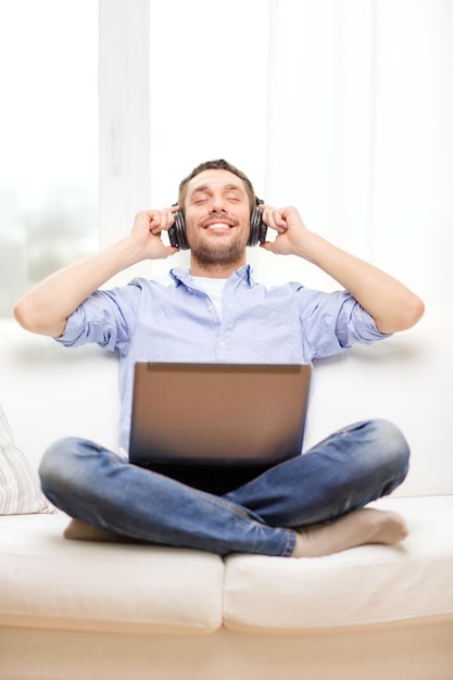 concetto di tecnologia, casa, musica e stile di vita - uomo sorridente con laptop e cuffie a casa