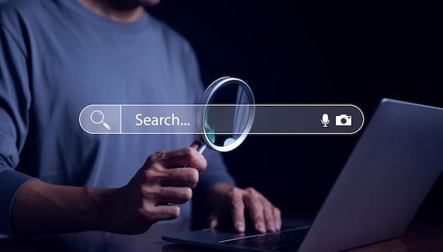 Concetto di tecnologia dei motori di ricerca Imprenditore che tiene in mano una lente d'ingrandimento e utilizza un computer portatile per cercare informazioni su Internet con il browser web Barra di ricerca di lavoro sul sito web Ricerca online