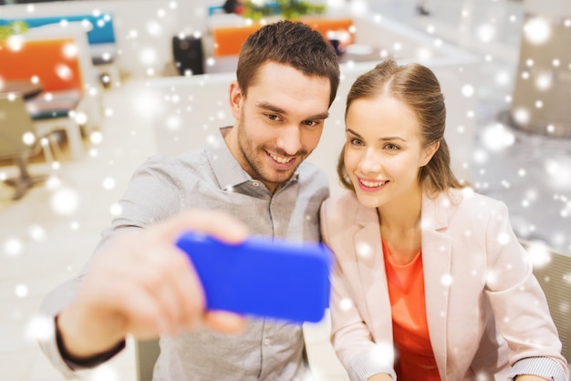 concetto di tecnologia e persone - coppia felice che si fa selfie con lo smartphone in centro commerciale o bar con effetto neve