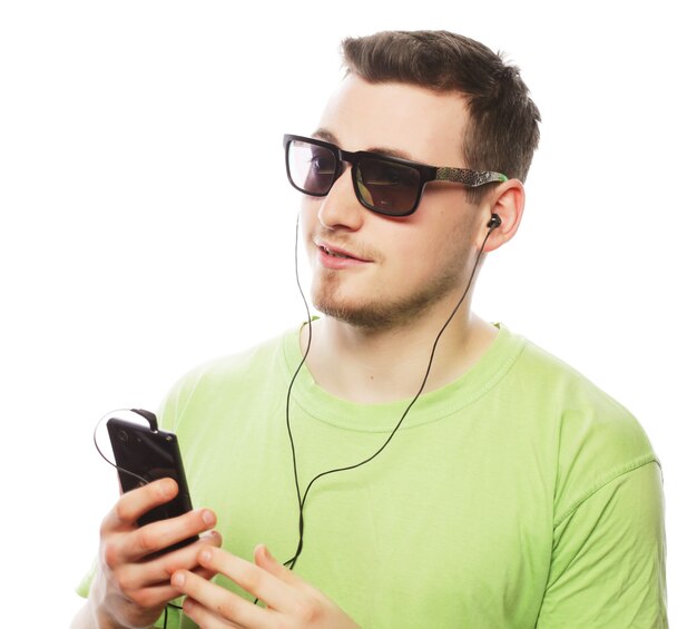 Concetto di tecnologia e persone. giovane uomo che indossa t-shirt verde ascoltando musica e utilizzando smartphone, isolato su bianco