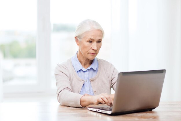 concetto di tecnologia, età e persone - donna anziana con computer portatile a casa