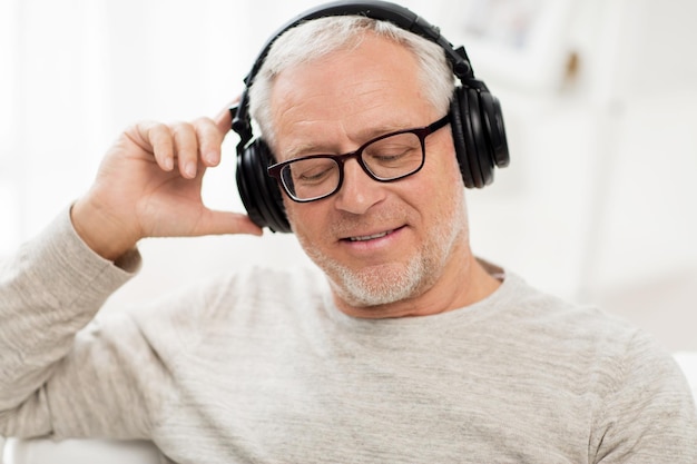 concetto di tecnologia, persone e stile di vita - primo piano di un uomo anziano felice in cuffia che ascolta la musica a casa