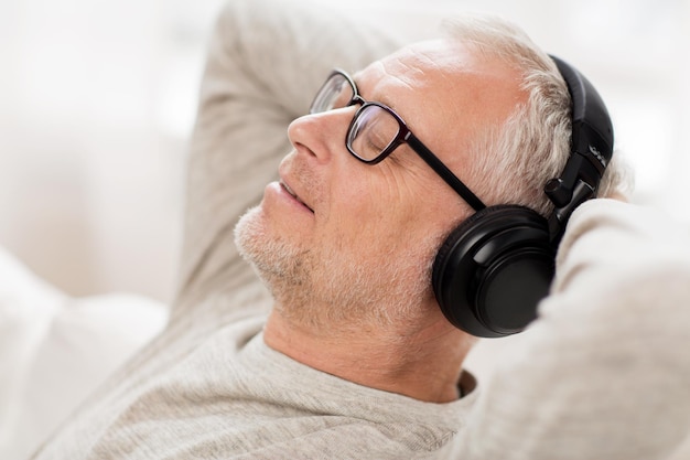 concetto di tecnologia, persone e stile di vita - primo piano di un uomo anziano felice in cuffia che ascolta la musica a casa